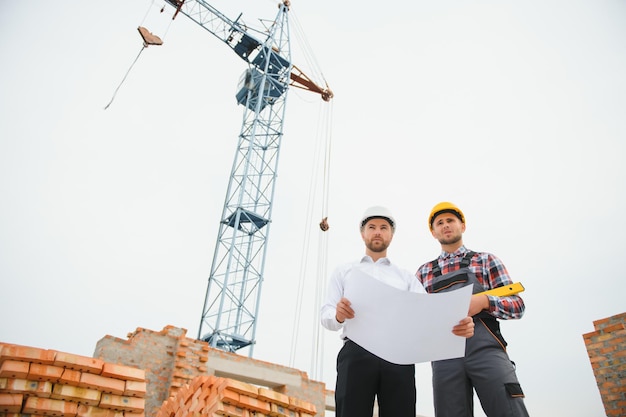 Construction engineers supervising progress of construction project stand on new concrete floor top roof and crane background