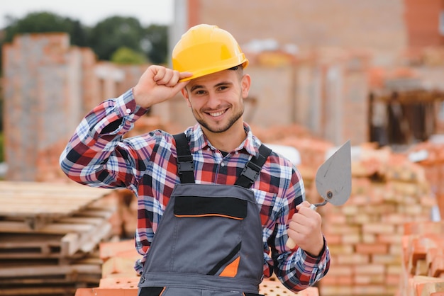 Construction mason worker bricklayer installing red brick with trowel putty knife outdoors