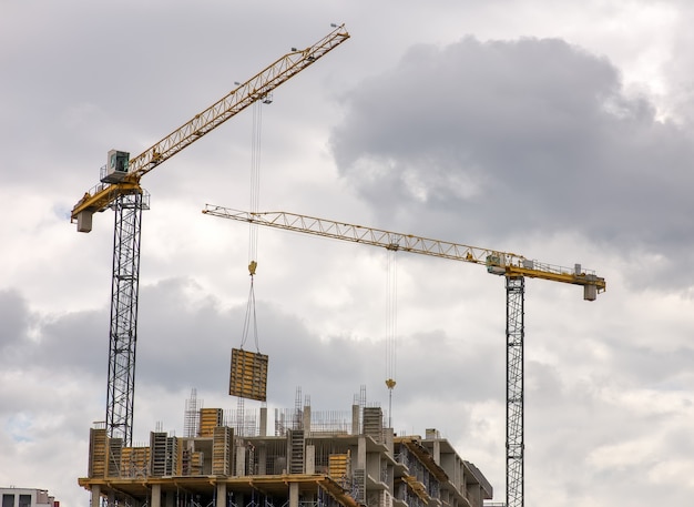 Construction of multi-storey buildings with Crane. Workers work on building object.