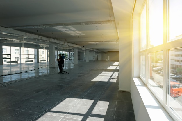 Construction and repair Two men with a cable in an empty room with white walls tiled floors and window sunny