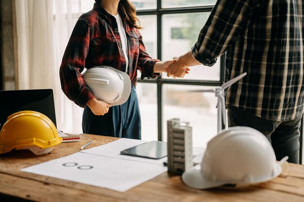 Construction team shake hands greeting start new project plan behind yellow helmet on desk in office center to consults about their building project