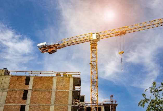 Construction tower crane on the construction site of a modern brick residential building against the background of sunlight sunrise summer