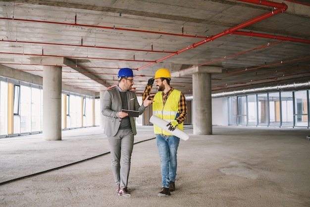 Construction worker and architect walking in building in construction process and discussing about project.