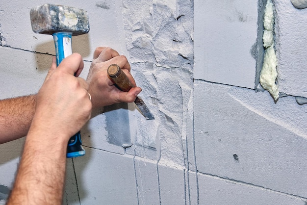 Construction worker gouges niche in concrete wall using hammer and chisel