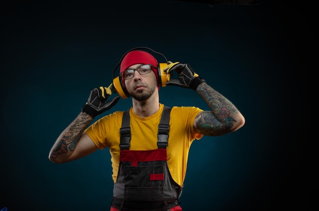 A construction worker guy in overalls wearing protective headphones on a dark background