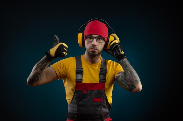 A construction worker guy in overalls wearing protective headphones on a dark background