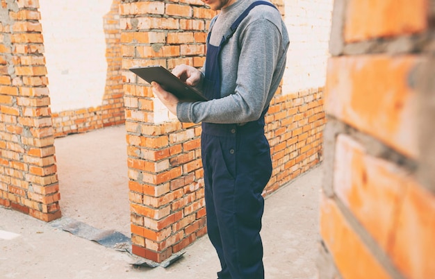 Construction worker standing in the house under construction and holding tablet computer