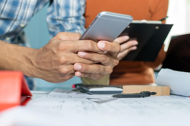 Construction worker team calculate on mobile smart phone and working on blueprint on desk in meeting room office at construction site, contractor, architecture, industrial, engineering concept