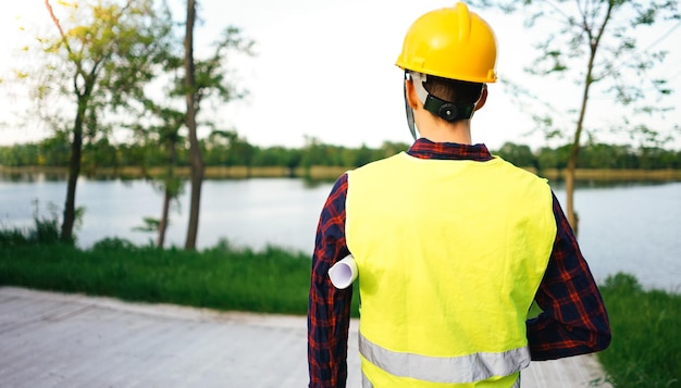 Construction worker wearing yellow vest staying in front of the lake Worker holding site schedule