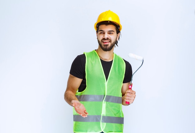 Construction worker with a yellow helmet holding a white trim roller.