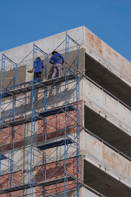 Construction workers on scaffolding plastering cement wall outside of high parking garage building