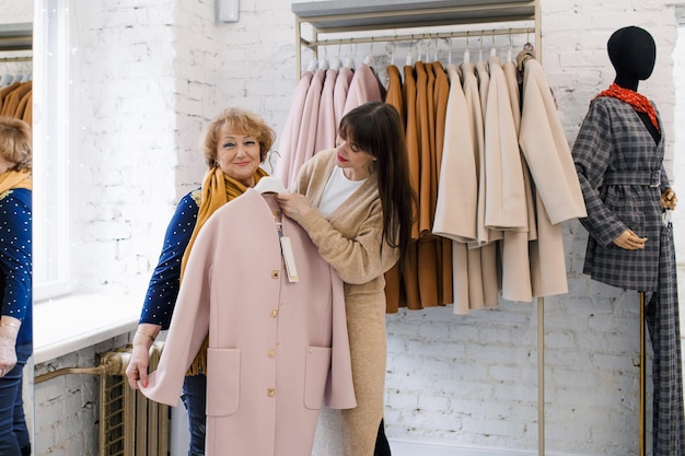 A consultant girl in a clothing store helps an elderly woman customer choose clothes Shopping