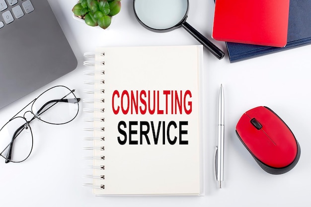 CONSULTING SERVICE text on a notepad with laptop on the white background