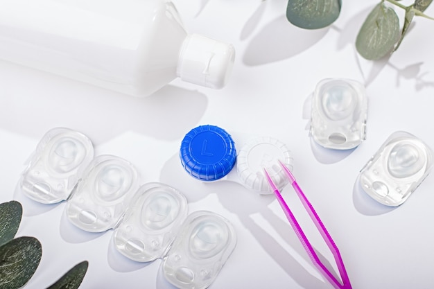 Contact lens kit with lenses, bottle of lens solution, case, tweezers on white table, top view