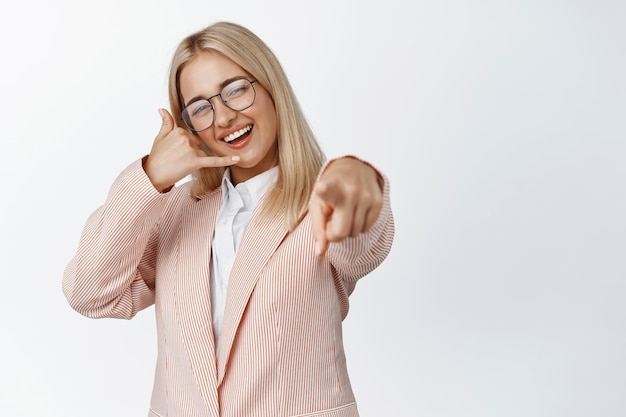 Contact us Smiling business woman pointing finger at camera and showing phone call gesture promoting her company white background