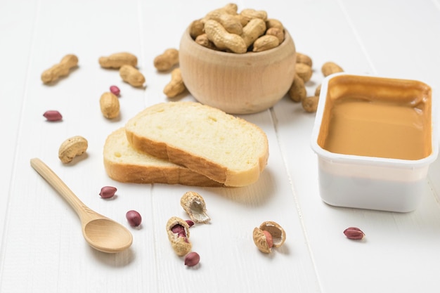 A container of peanut paste and white bread on a white table