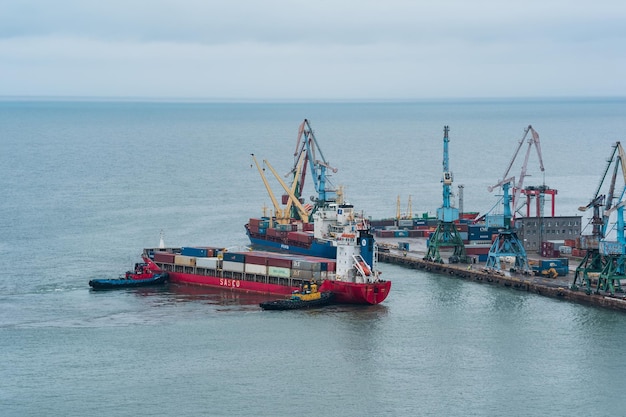 Container ship is moored with the help of tugboats to a cargo berth