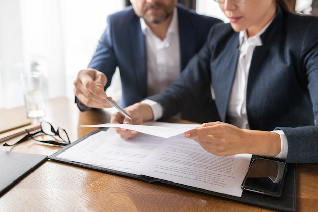 Contemporary businessman pointing at paper held and read by young Asian woman by table in restaurant