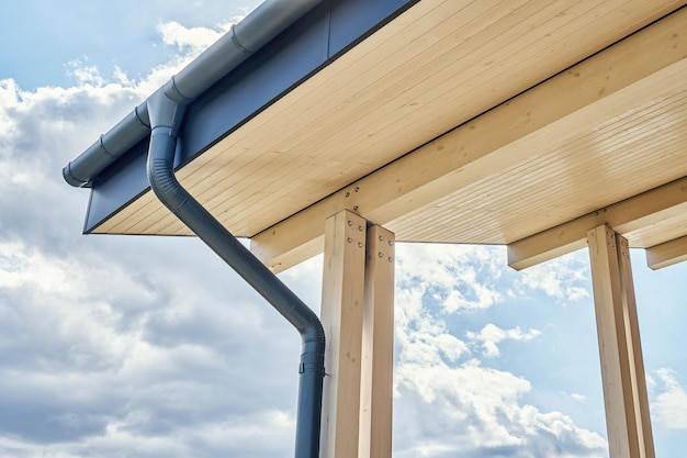 Contemporary grey metal rainwater downpipe installed on roof of new building on cloudy day closeup