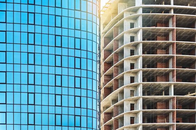 Contemporary skyscraper building with blue glass facade and highrise carcass at construction site