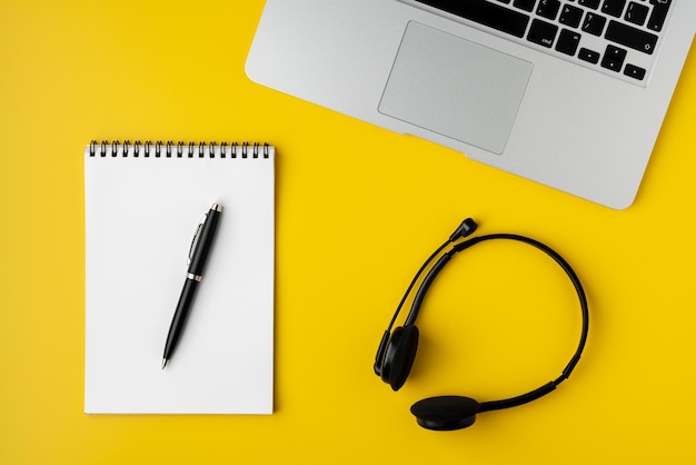 Contemporary workspace on yellow background notebook with pen laptop and digital headset