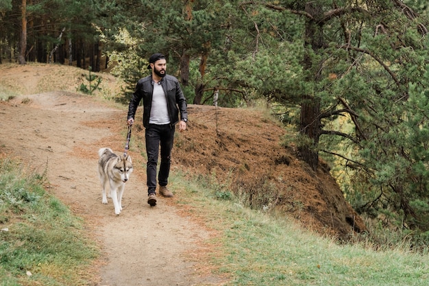 Contemporary young man in casualwear walking down footpath while holding leash of his purebred dog