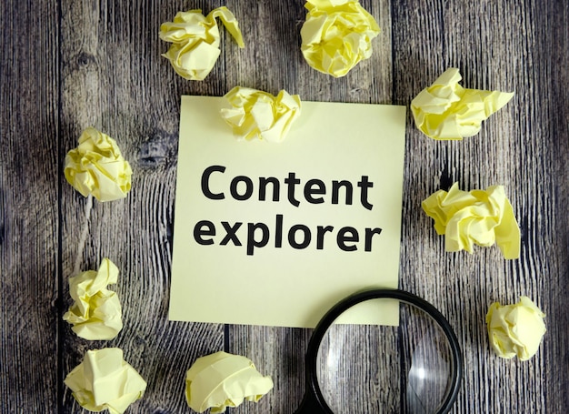 Photo content explorer seo concept - text on yellow note sheets on a dark wooden surface with crumpled sheets and a magnifying glass