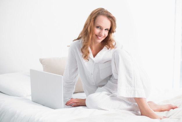 Content pretty woman using a laptop sitting on her bed