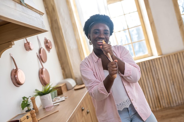 Contented african woman in pink clothes singing in the kitchen