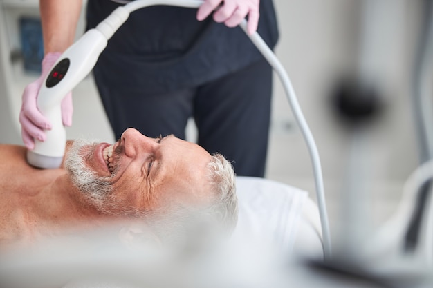 Contented elderly citizen smiling while undergoing an ultrasonic cavitation treatment at clinic