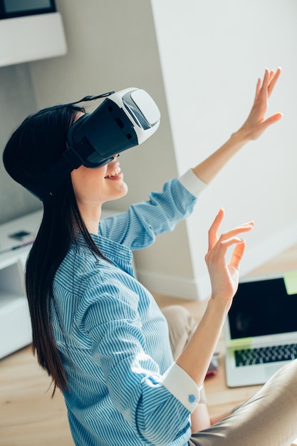 Contented long haired young woman smiling and putting hands in the air while using virtual reality device