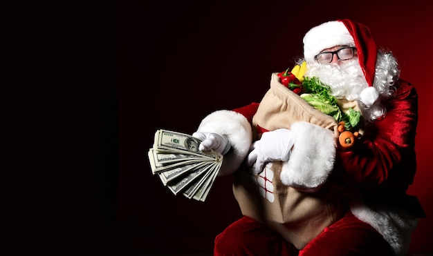 Contented Santa Claus holds a large bag full of fruits and vegetables and a bundle of 100 dol