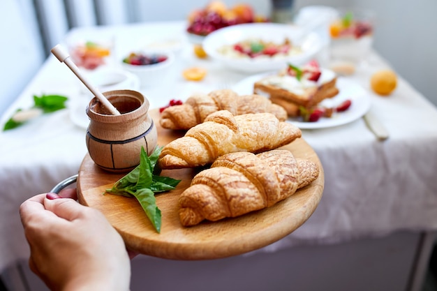 Continental breakfast table served with traditional French croissant in woman hand