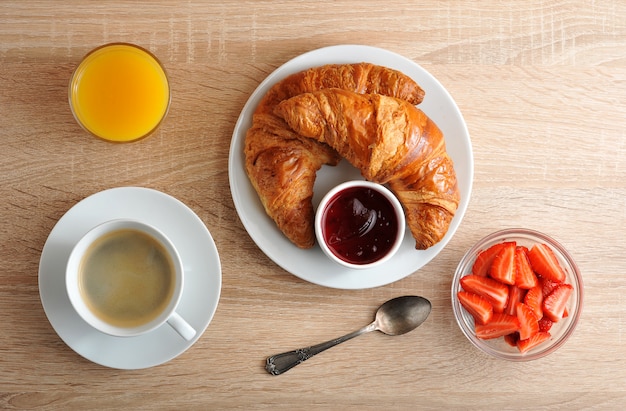 Continental Breakfast with coffee, croissant with jam, strawberries and orange juice on wooden surface