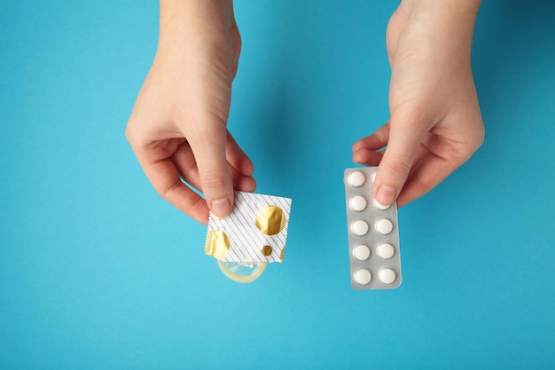 Contraceptive means a condom and birth control pills in a hand on a blue background