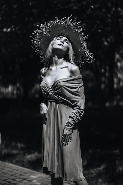 Contrasting black and white portrait of a sexy glamorous girl in a hat and dress in nature. With film grain, noise