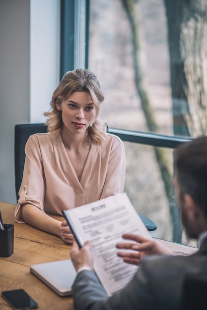 Conversation. Serious young blonde business woman and man in suit with papers discussing cooperation sitting in office