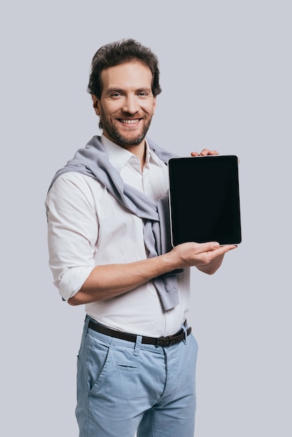 Convinient way of connection. Beautiful young man in smart casual clothes holding digital tablet and smiling while standing 