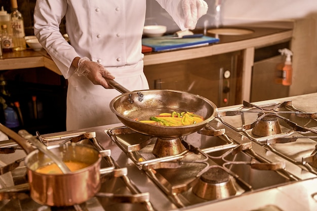 Cook adding salt to a frying pan with vegetables