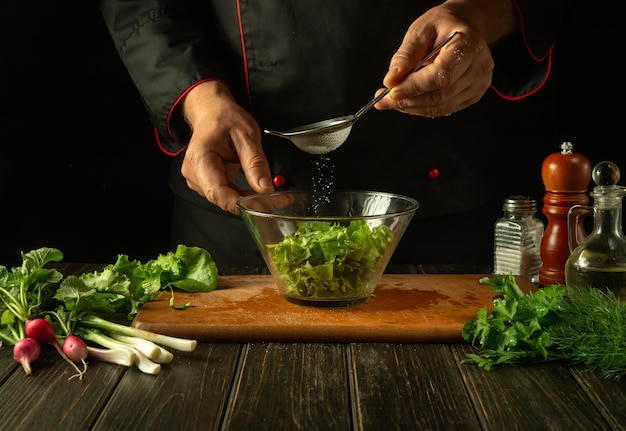 The cook adds pepper to the vegetable salad Vegetarian food by the hands of the chef in the kitchen Vegan menu idea for a hotel or restaurant