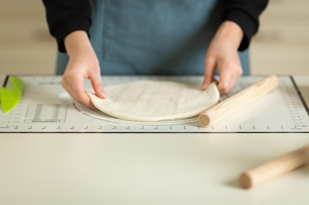 A cook in a blue apron takes rolled out dough from a kitchen silicone baking mat View of hands and workspace copy space