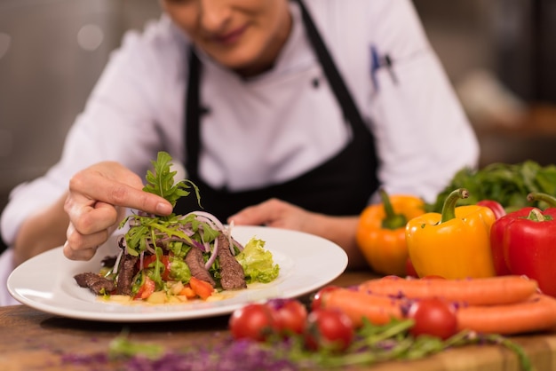 cook chef decorating garnishing prepared meal dish on the plate in restaurant commercial kitchen