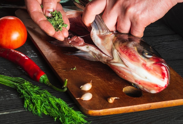 Cook or chef prepares fresh fish bighead carp with add spice. Preparing to cook fish food. Working environment in the restaurant or cafe kitchen