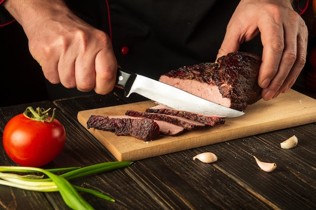 Photo the cook cuts the baked veal meat on a cutting board