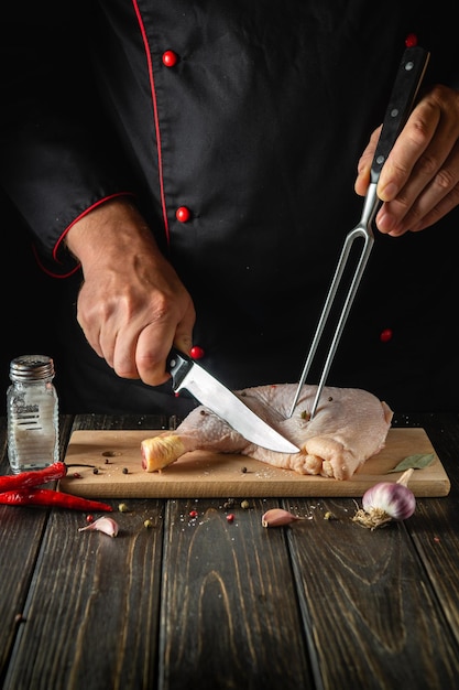 The cook cuts the chicken leg with a knife in the kitchen