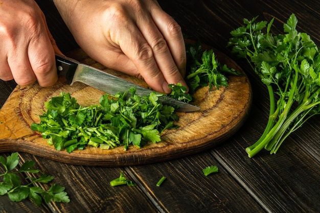 Cook cutting green parsley on a cutting board with a knife for preparing a vegetarian dish