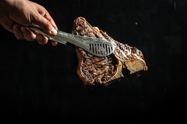 Cook hand with large piece of fresh beef meat prepared on a grill