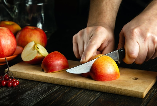 The cook hands with a knife slicing apples on a cutting wooden board for making delicious fruit drink The idea of the apple diet Copy space