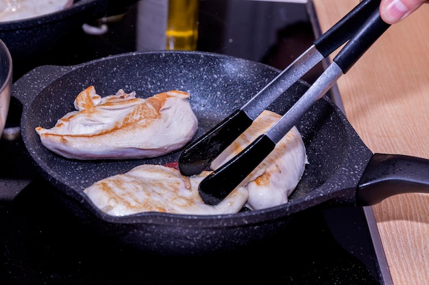 The cook is frying chicken meat fillet in a frying pan.