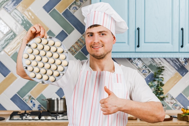 The cook in the kitchen holds dumplings in his hands and points at them with his hand The concept of cooking